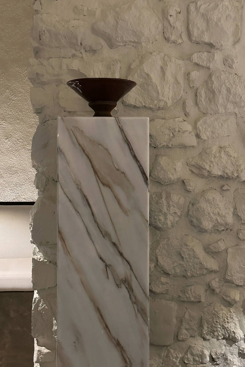 Peça de cerâmica em pedestal de mármore junto a parede de pedra